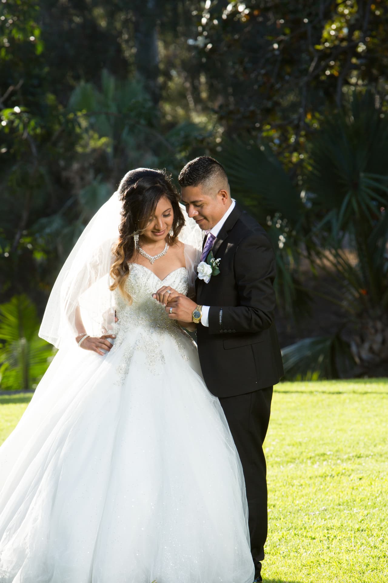 Bride and groom admiring her wedding ring in a sunlit garden