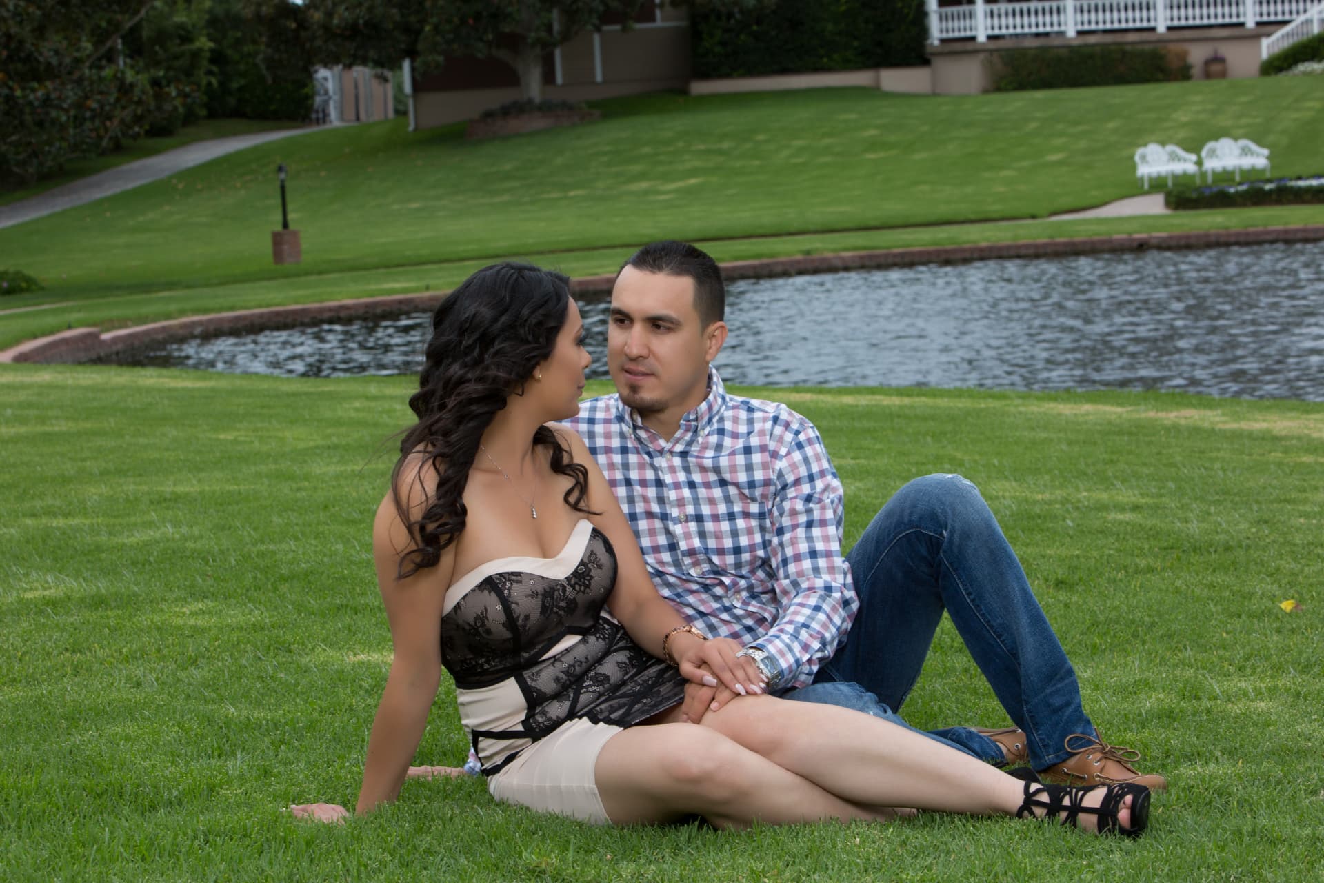 Engaged couple seated together on a green lakeside lawn