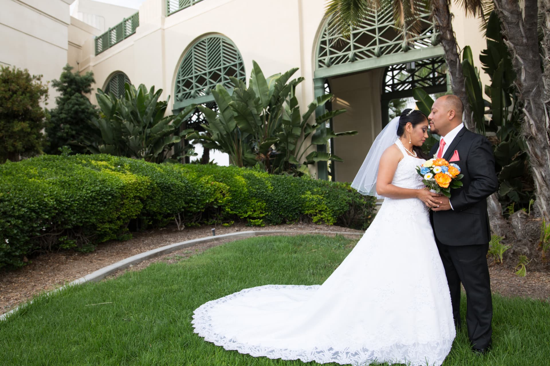 Bride and groom embracing beside tropical gardens and arched architecture