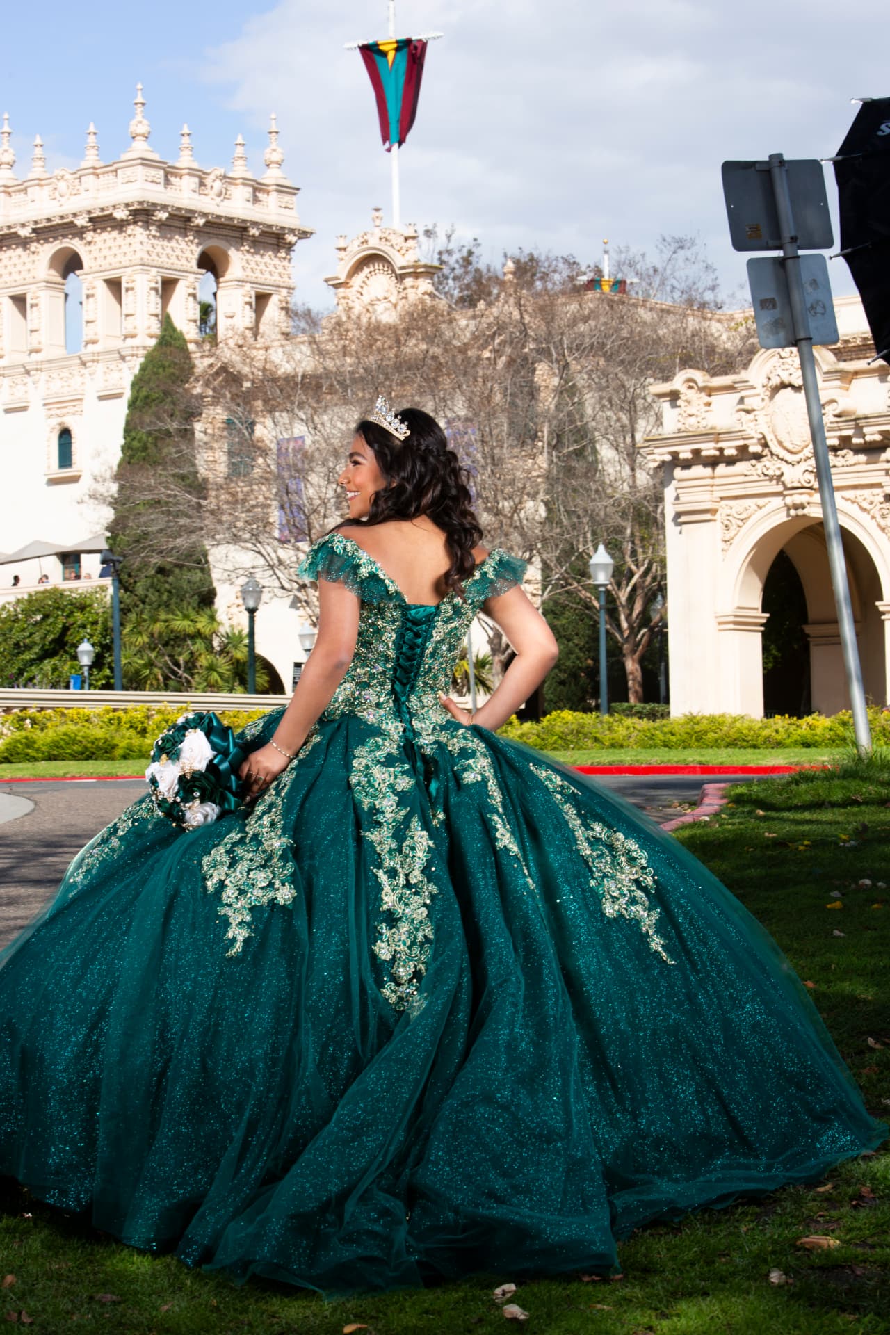 Quinceañera in an emerald and gold ball gown turning to look over her shoulder