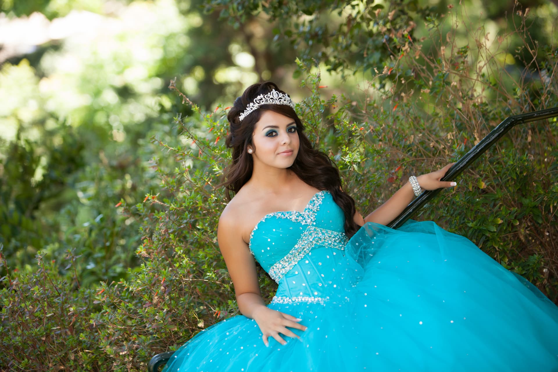 Quinceañera in a turquoise gown seated among the garden greenery