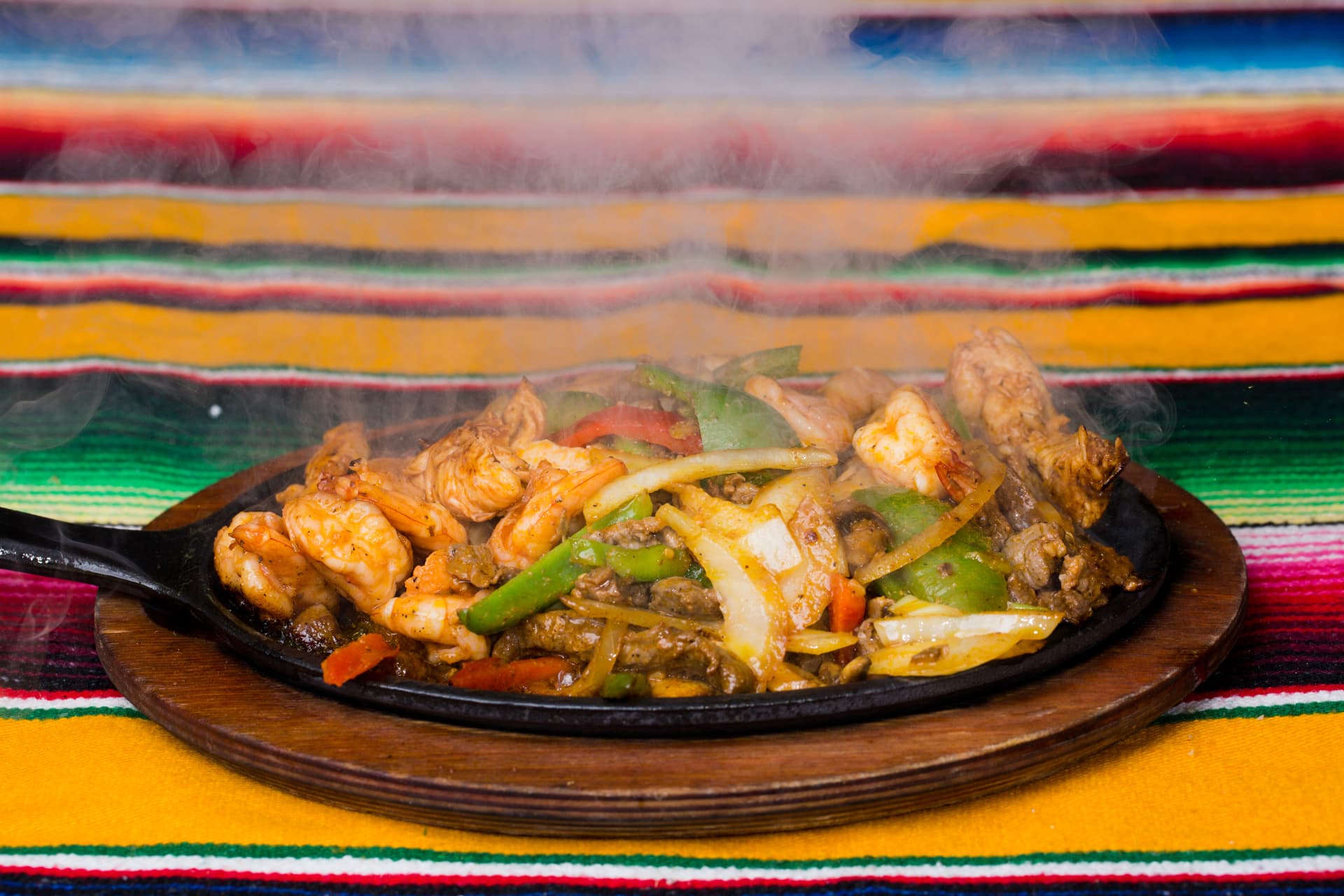 Steaming mixed fajitas with shrimp, beef, peppers, and onions on a sizzling skillet