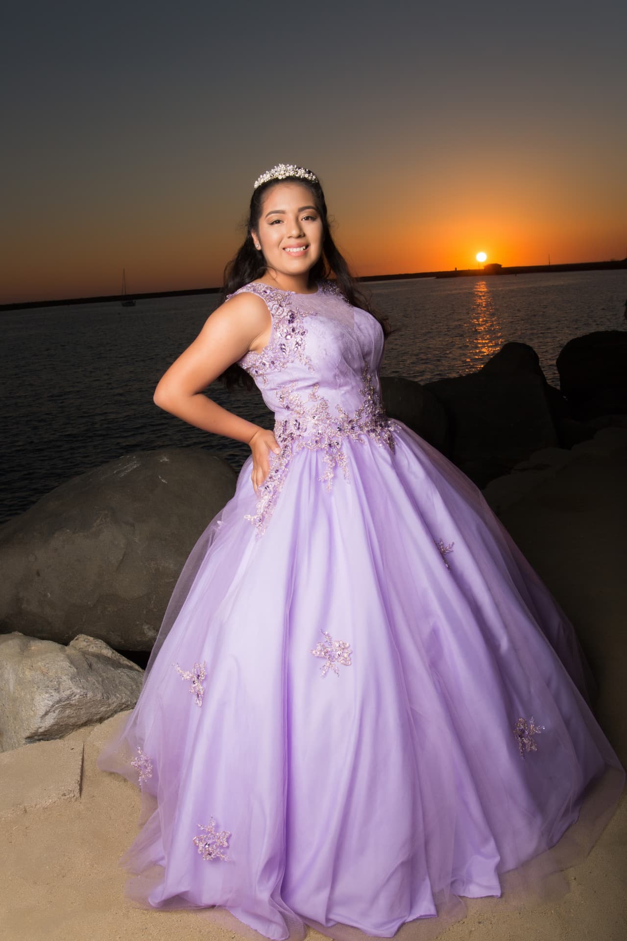 Quinceañera in a lavender embroidered gown posing on the beach at sunset
