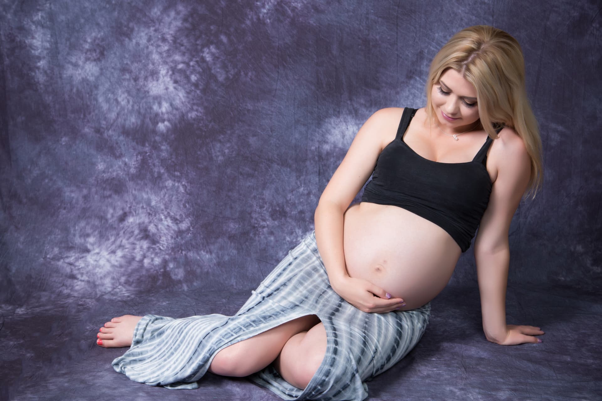 Expectant mother seated in a studio and looking lovingly at her baby bump