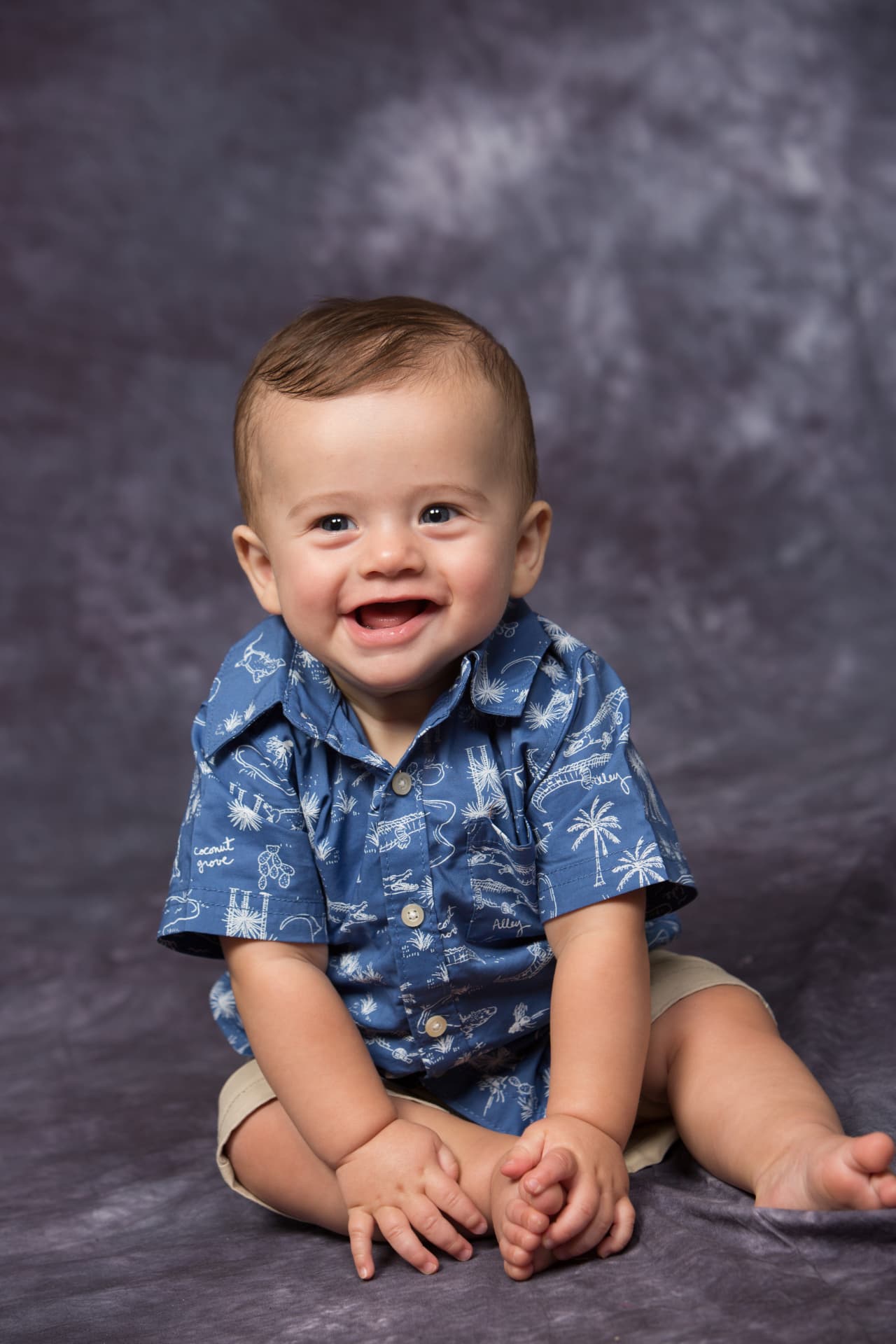 Joyful baby boy seated in a blue patterned shirt for a studio portrait