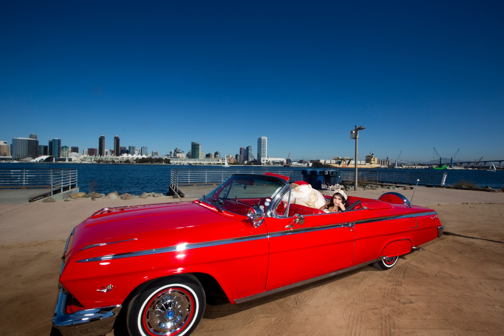 Quinceañera in a red convertible lowrider with the downtown San Diego skyline behind her