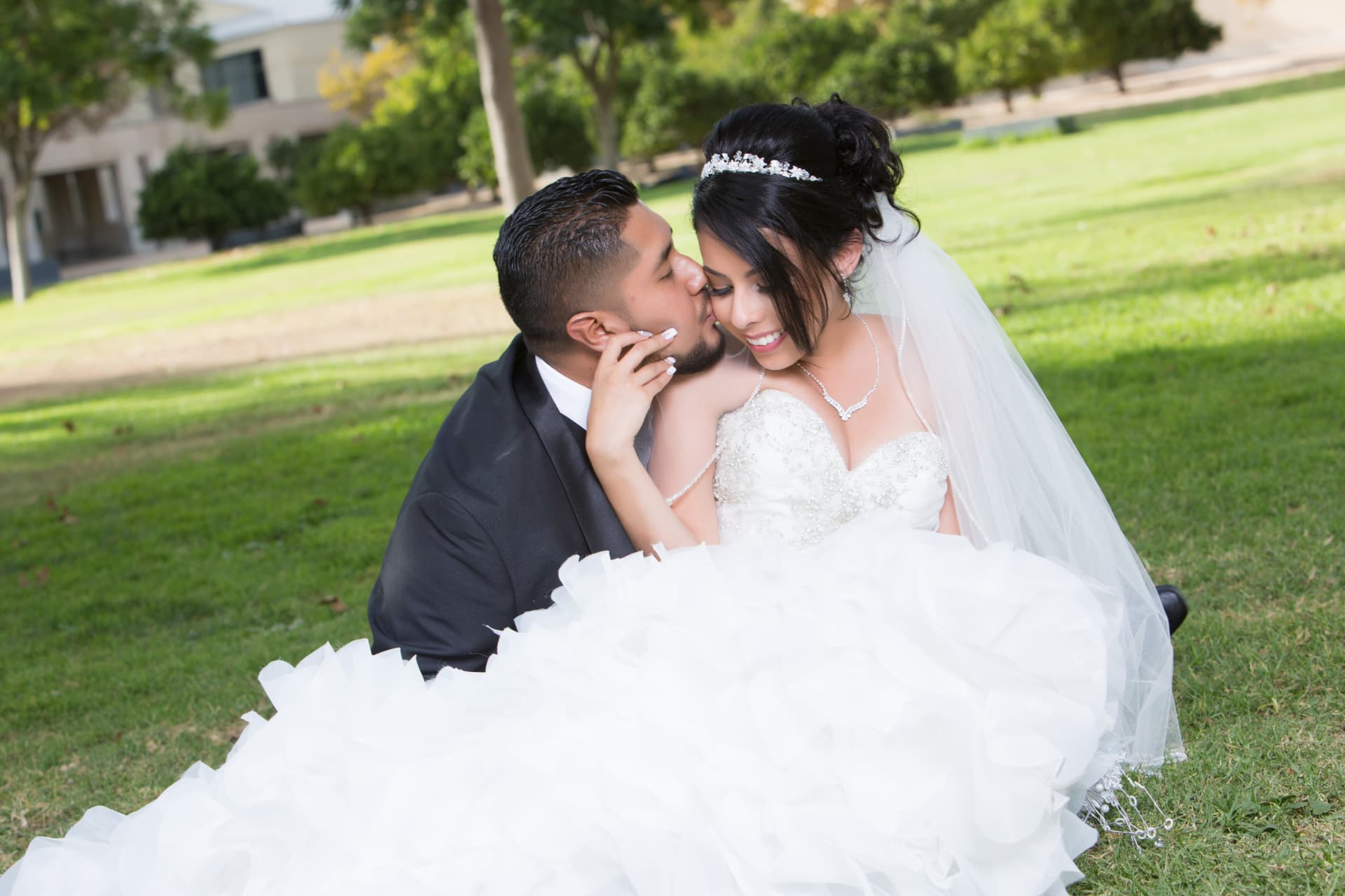 Groom kissing his smiling bride as they sit together on the grass