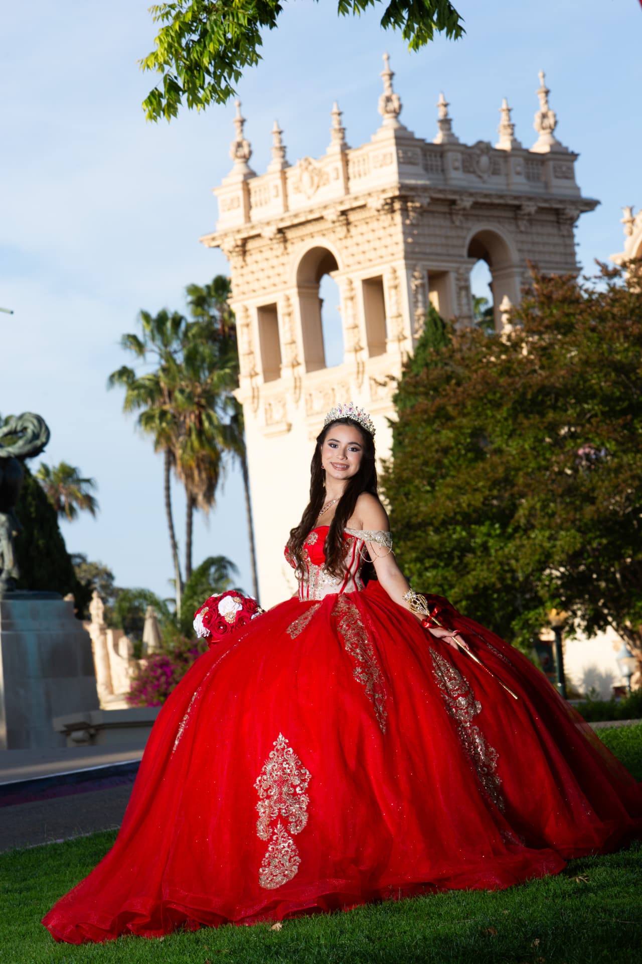 Quinceañera in a red gown with her scepter before the Balboa Park tower