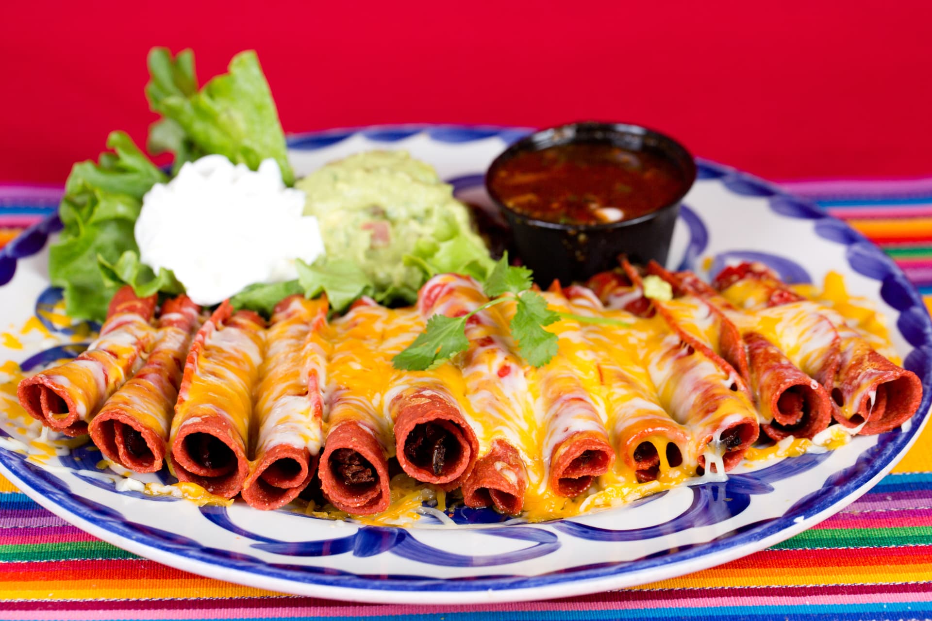 Cheese-topped taquitos served with guacamole, crema, lettuce, and salsa