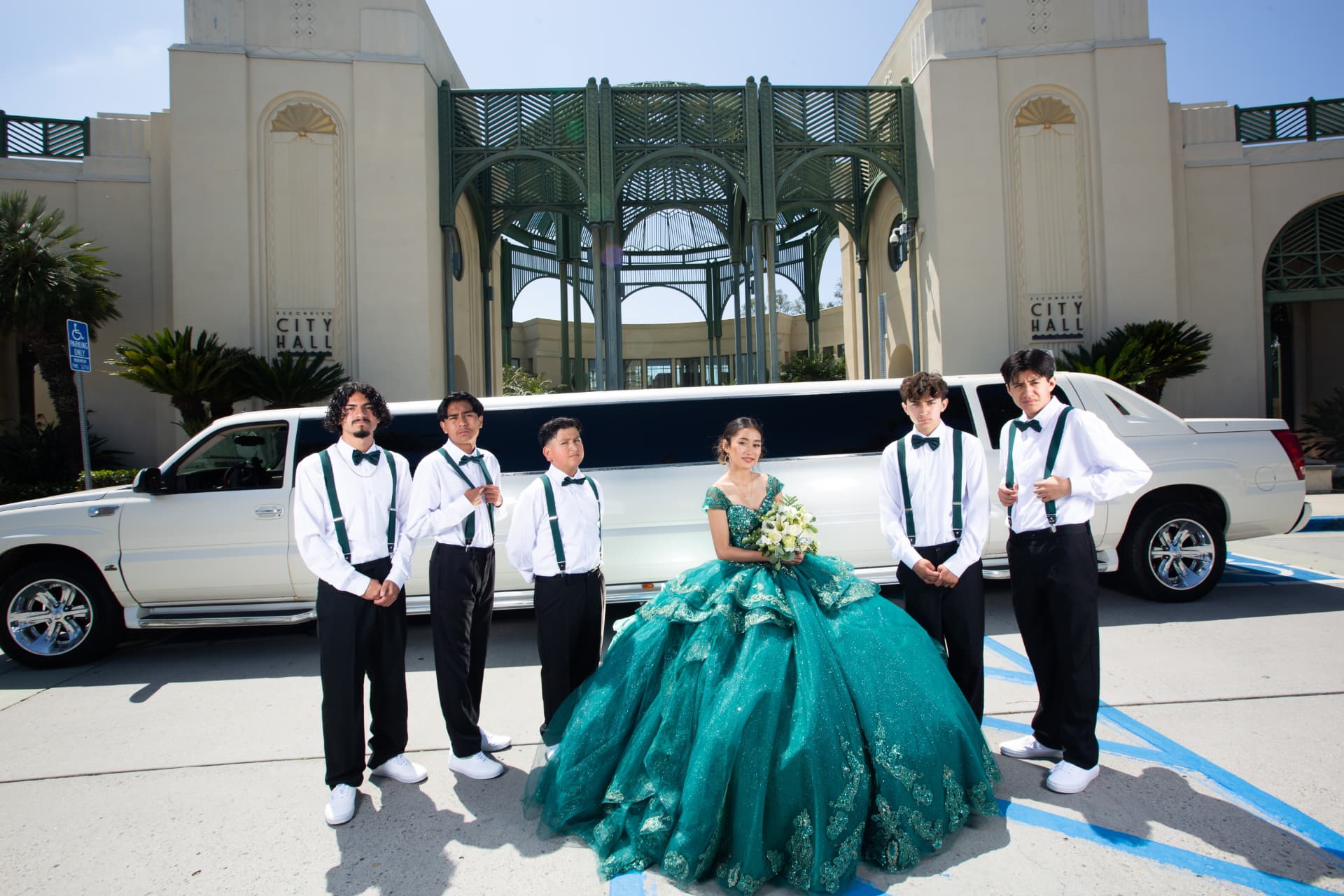 Quinceañera in an emerald green gown with her chambelanes in front of a white limousine