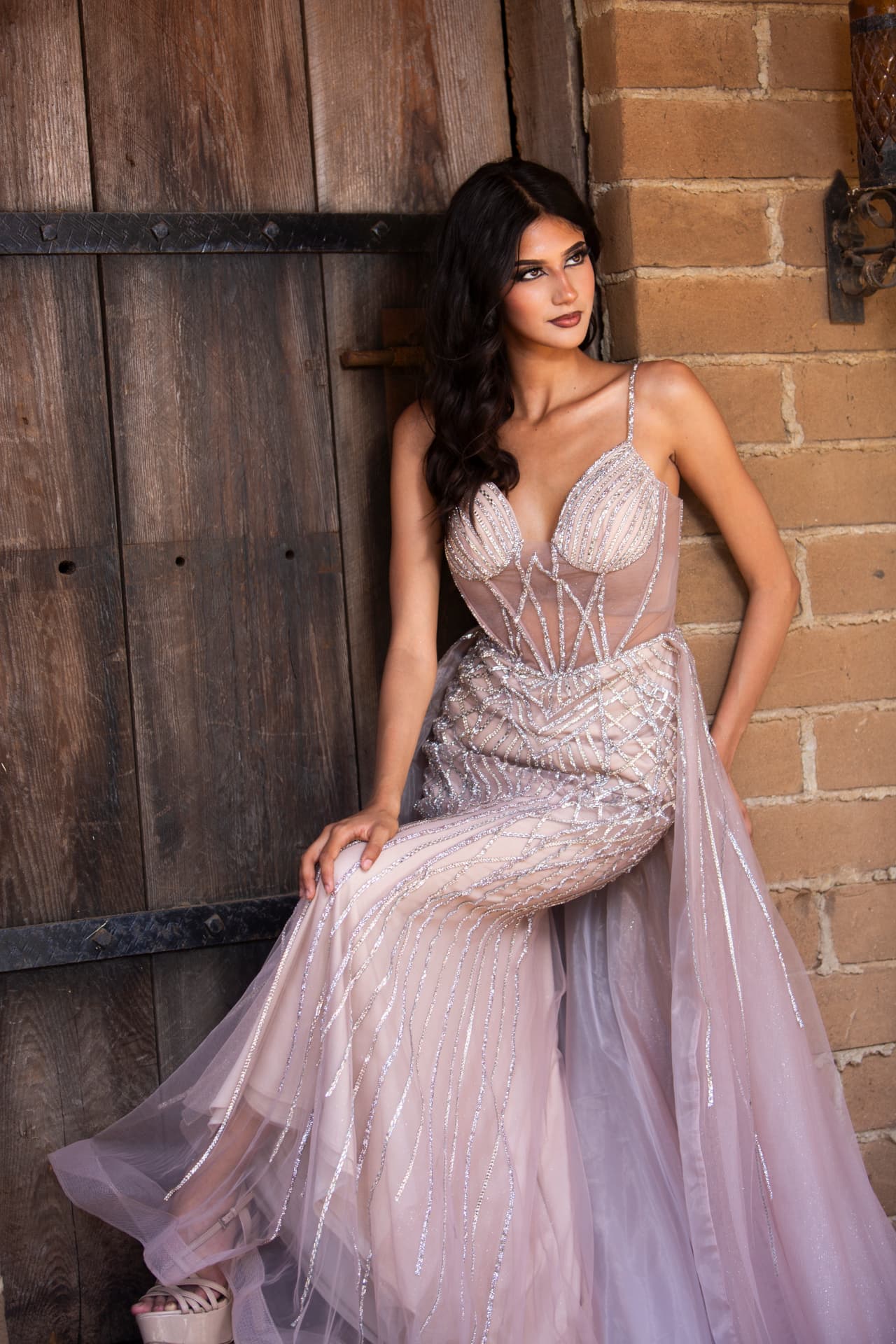 Seated fashion portrait in a blush jeweled gown beside a wooden door