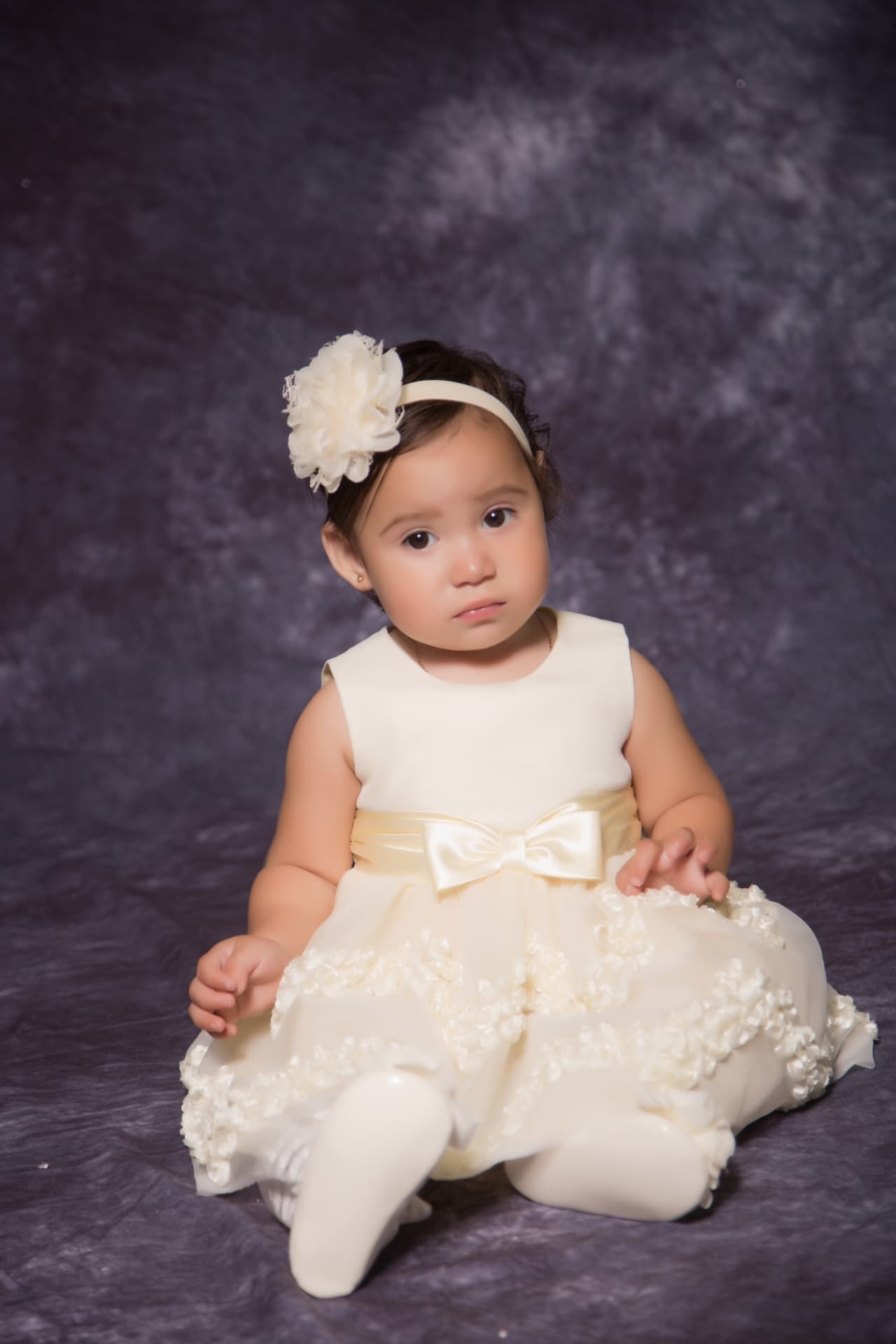 Baby girl in an ivory floral dress and flower headband seated for a studio portrait
