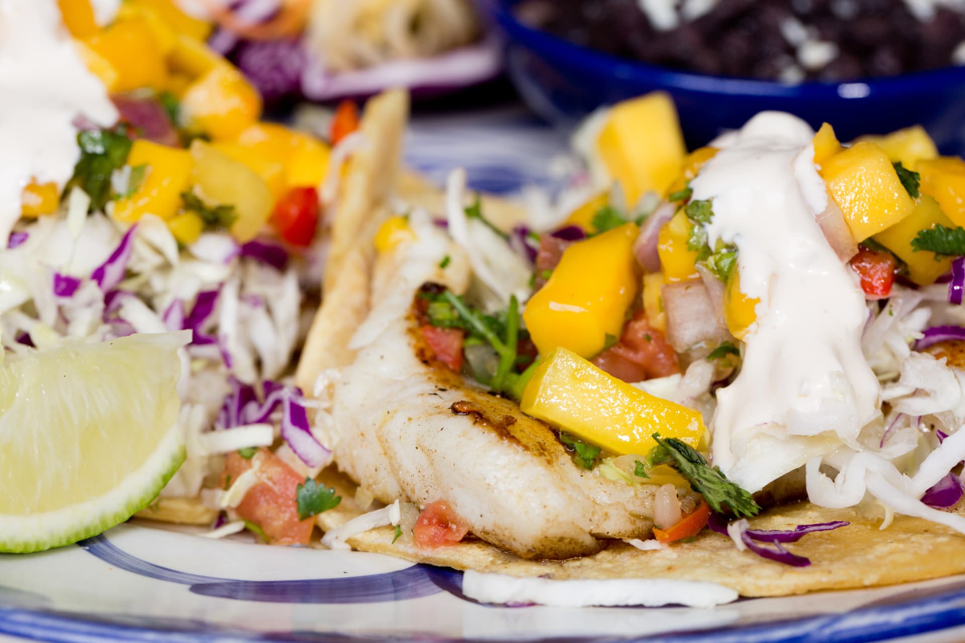 Grilled fish tacos topped with mango salsa, cabbage, crema, and fresh lime