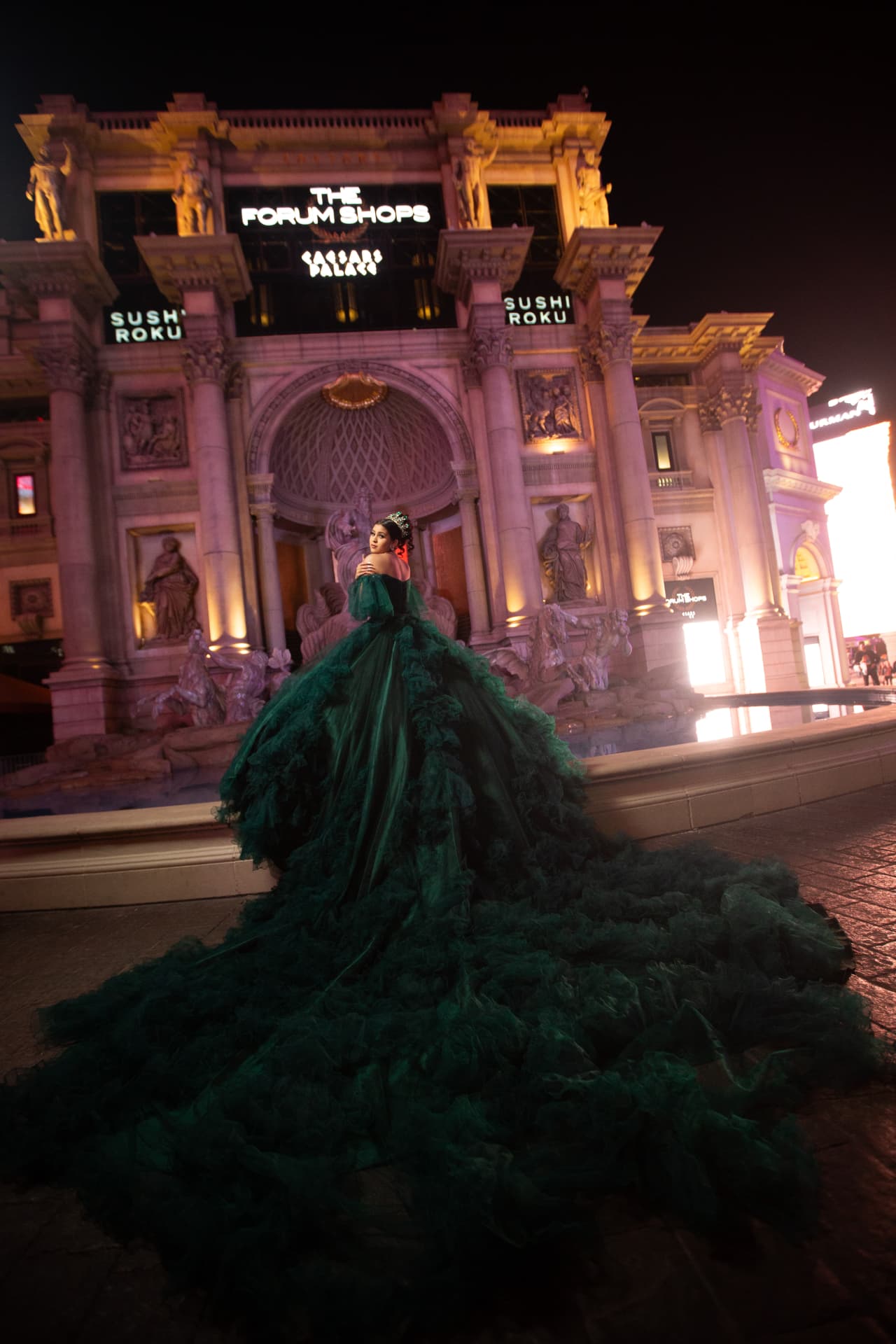 Quinceañera in an emerald green gown with a long train in front of the Forum Shops fountain in Las Vegas