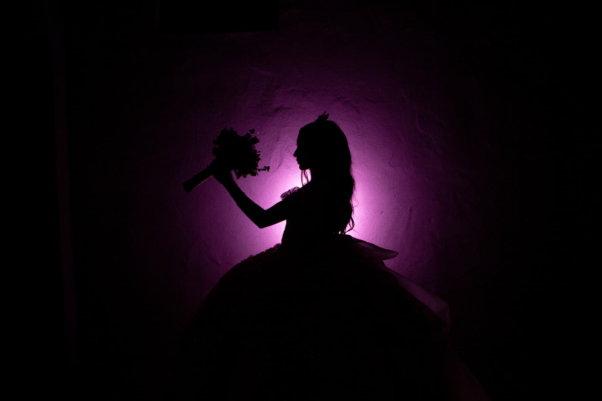 Quinceañera silhouette holding her bouquet up against a dramatic purple-lit wall
