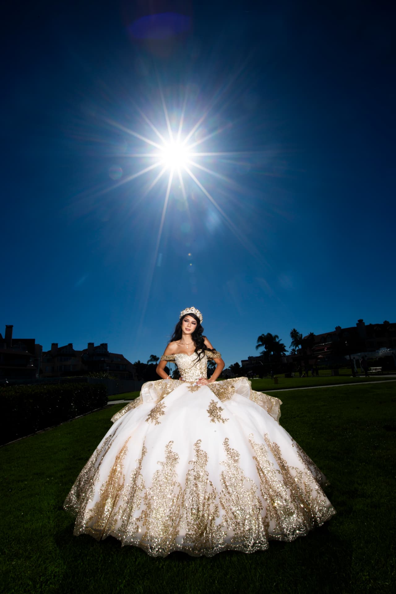 Quinceañera in a white and gold gown with the sun flaring above her at twilight