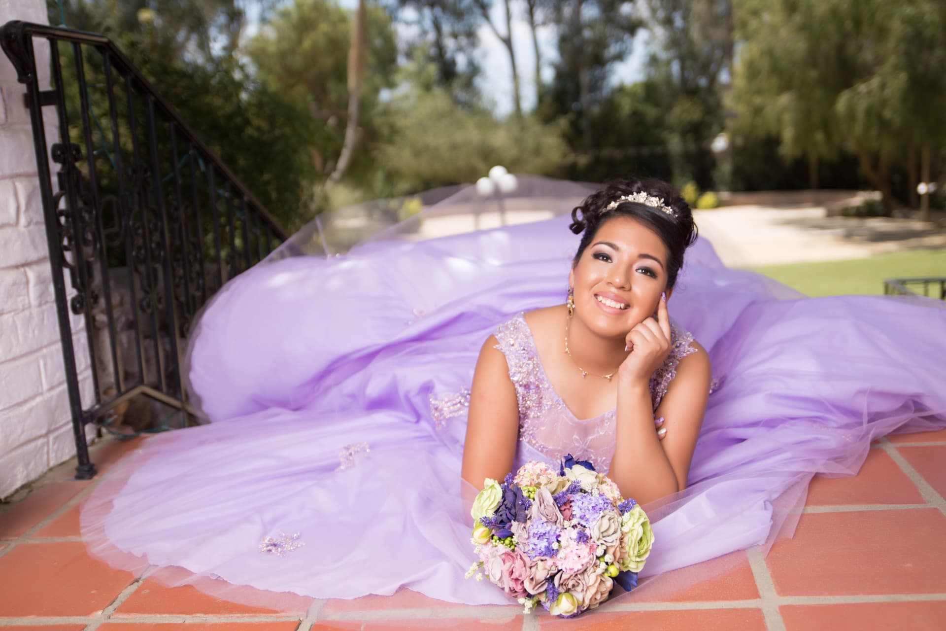 Quinceañera in a lavender gown lying on a brick terrace with a pastel bouquet
