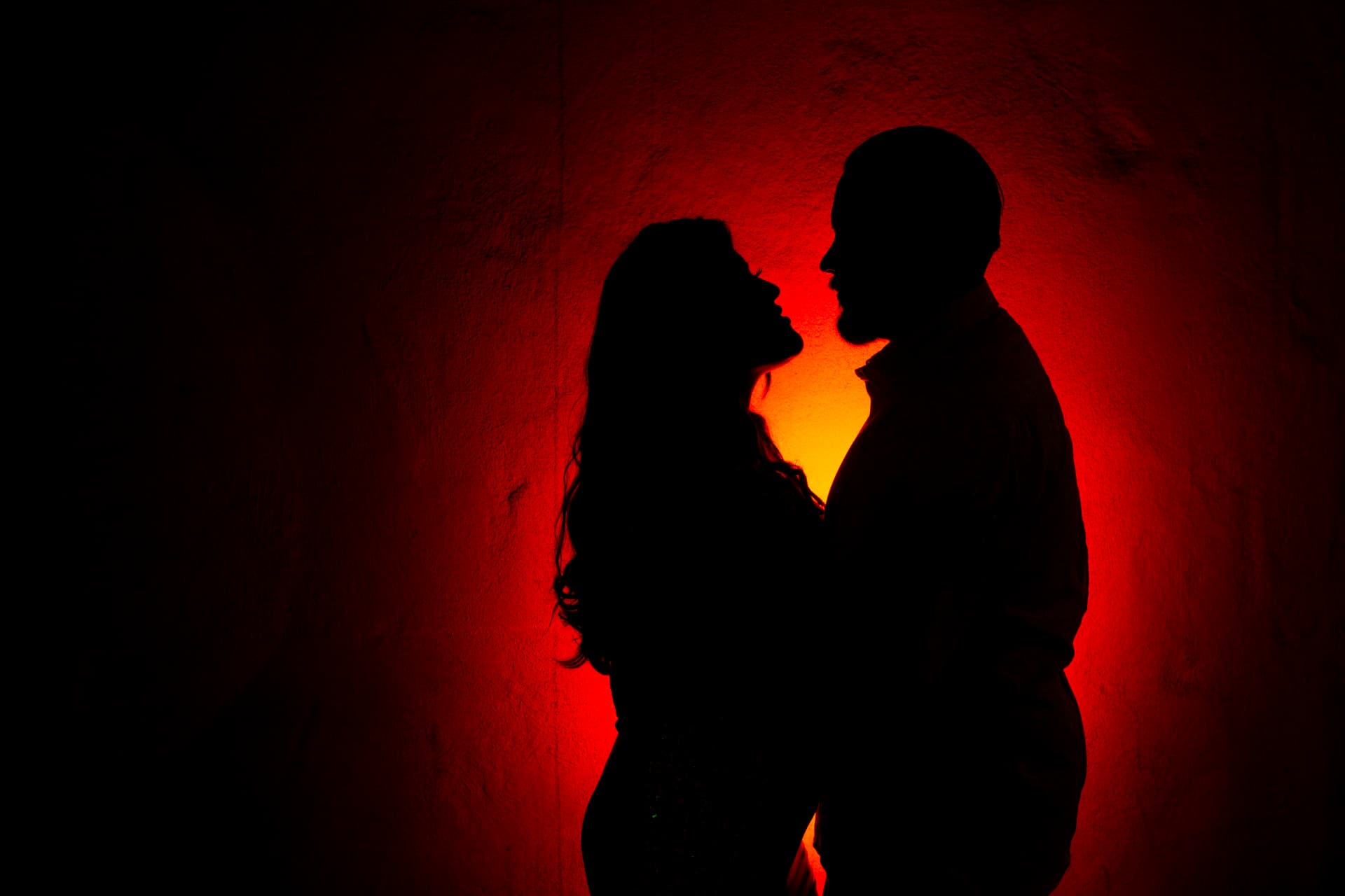 Engaged couple silhouetted against vivid red and amber light