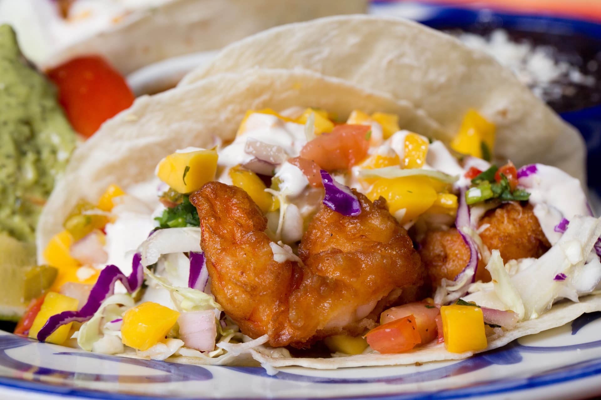 Crispy shrimp taco topped with mango salsa, cabbage, crema, and cilantro