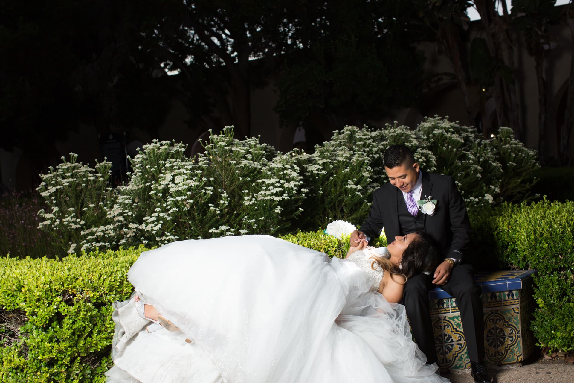 Bride reclining across her groom’s lap on a colorful tiled garden bench
