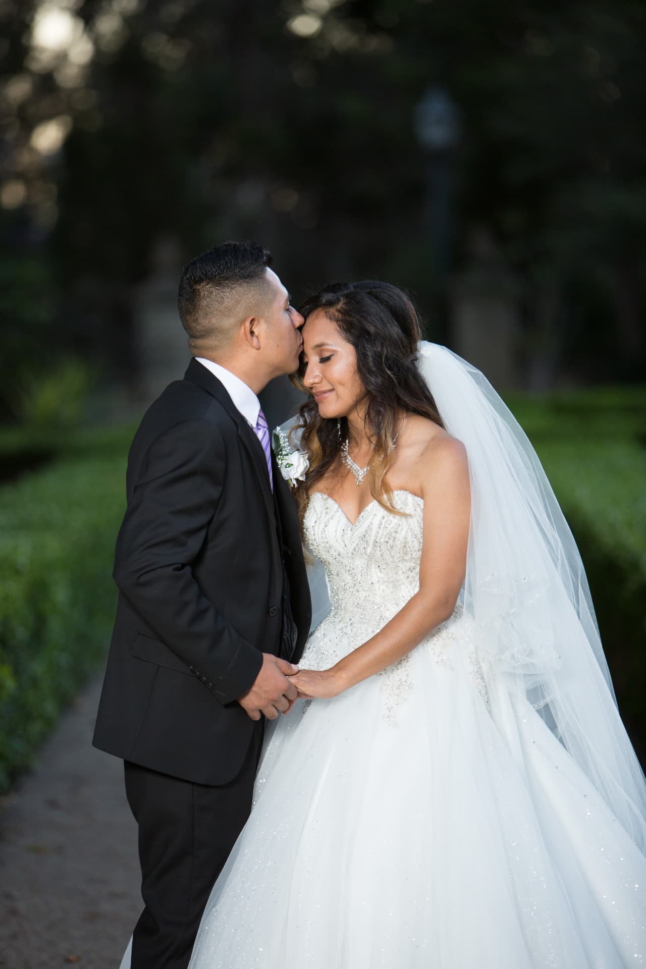 Groom kissing his bride’s forehead during a quiet garden portrait