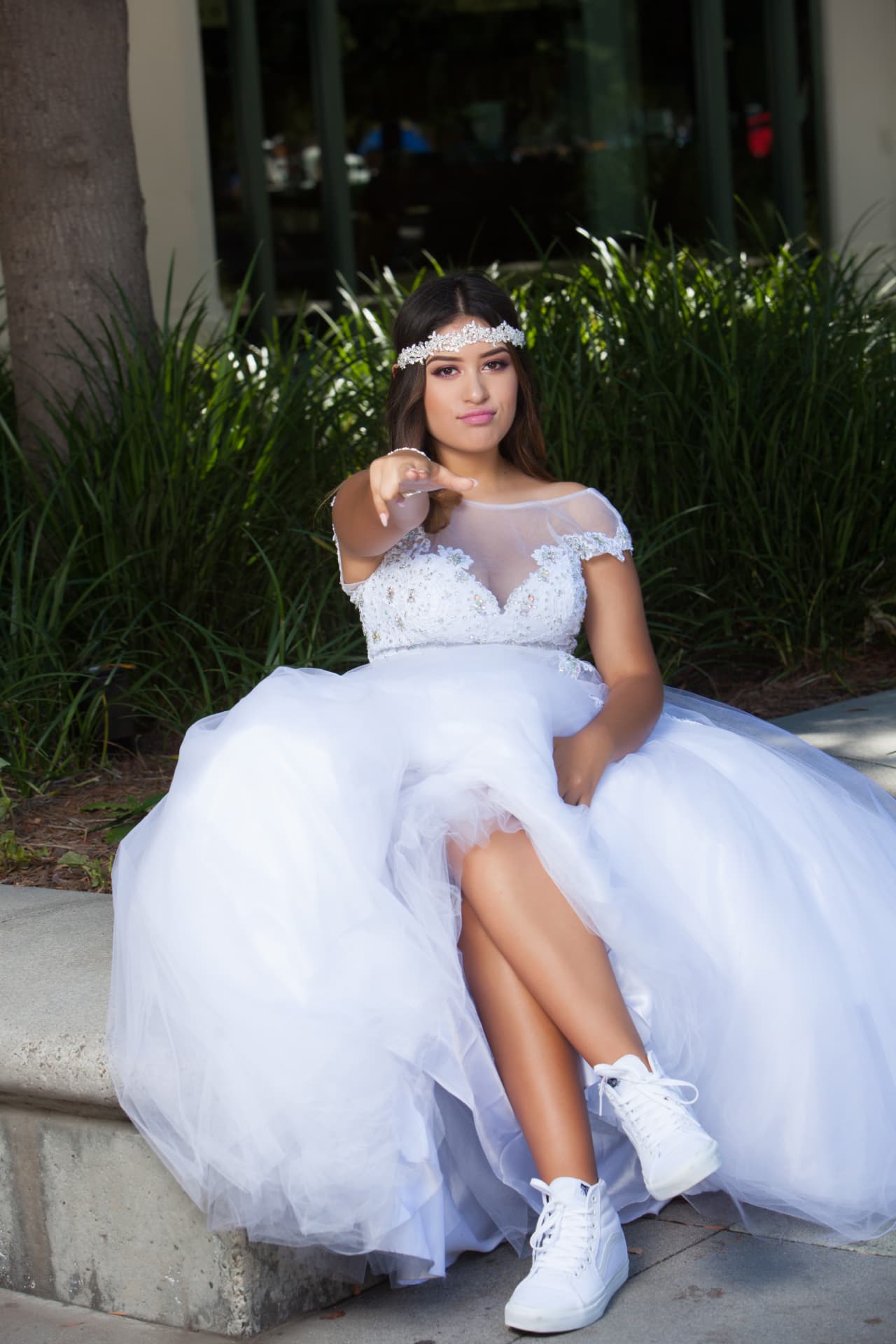 Quinceañera in a white gown and tiara headband with white sneakers reaching her hand toward the camera