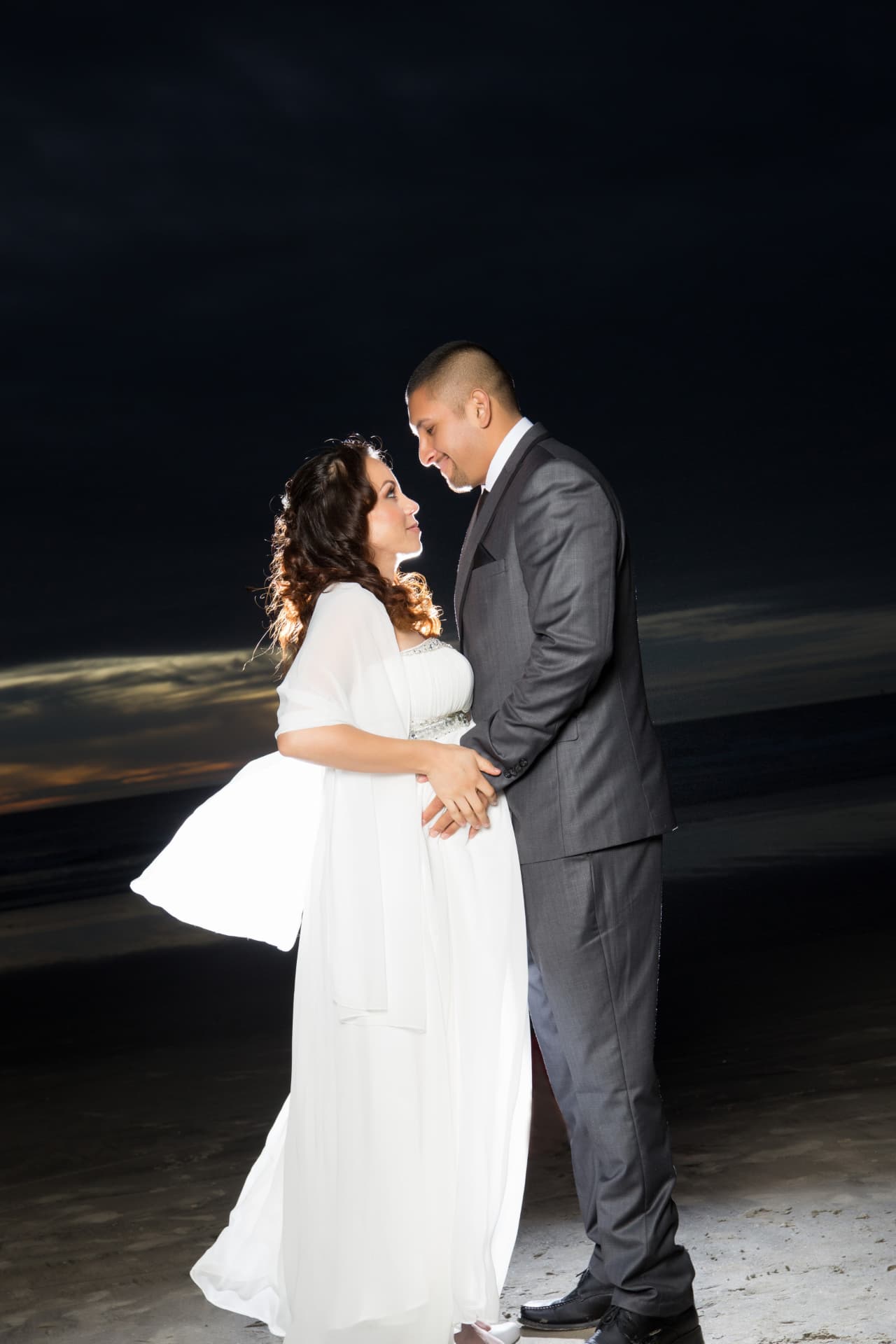 Bride and groom holding hands in an intimate beach portrait beneath a dark evening sky