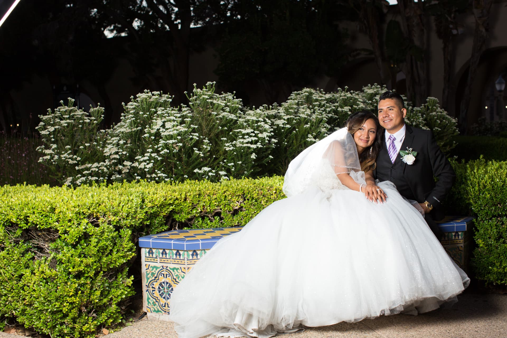 Bride and groom seated together on a colorful tiled garden bench