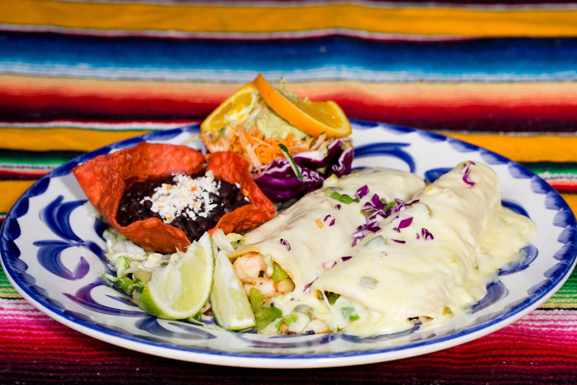 Seafood enchiladas covered in creamy sauce with black beans, cabbage, and citrus