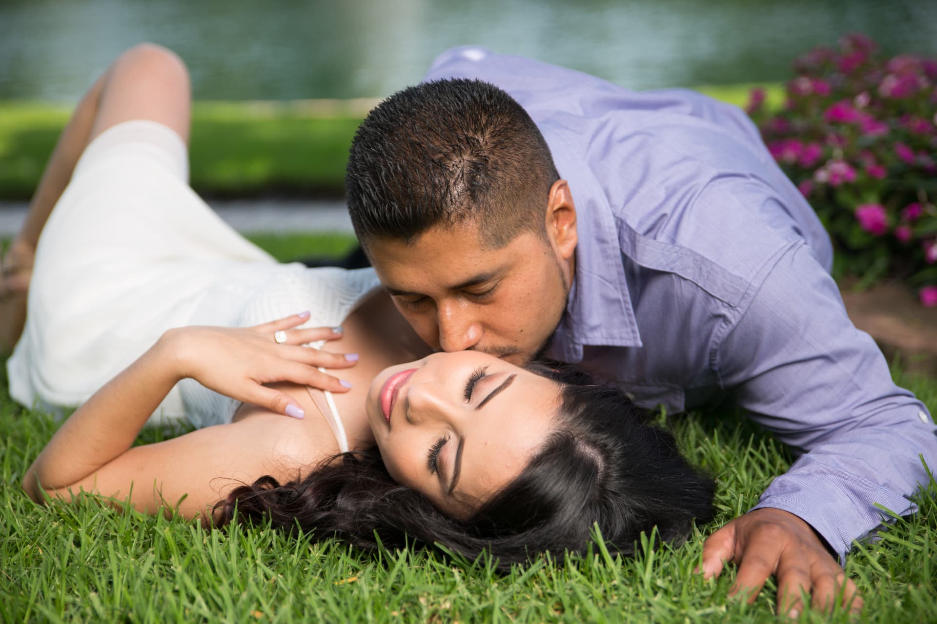 Engaged couple sharing a tender moment while reclining on a garden lawn