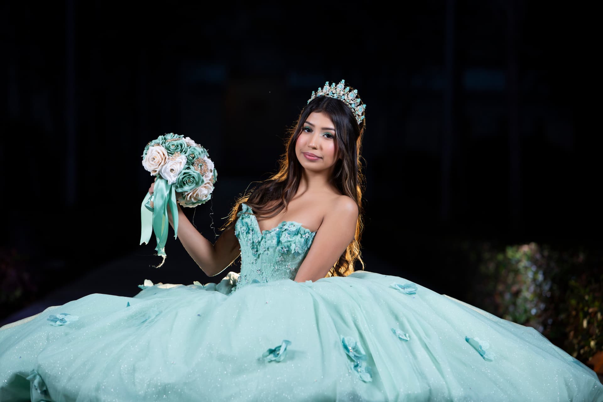 Quinceañera in a mint green gown with her tiara holding up a pastel bouquet in rim light