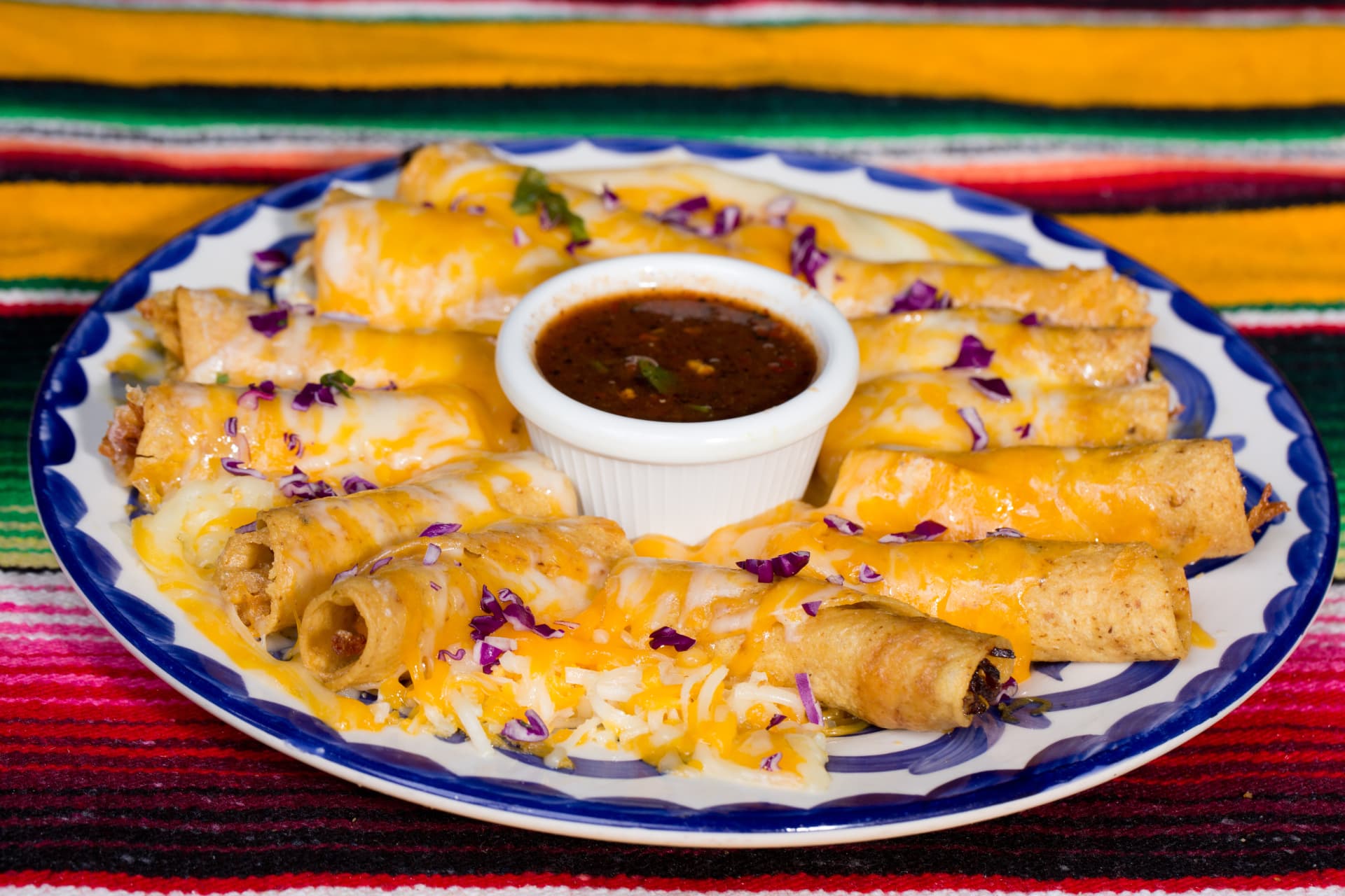 Crispy taquitos covered with melted cheese and served around a bowl of salsa
