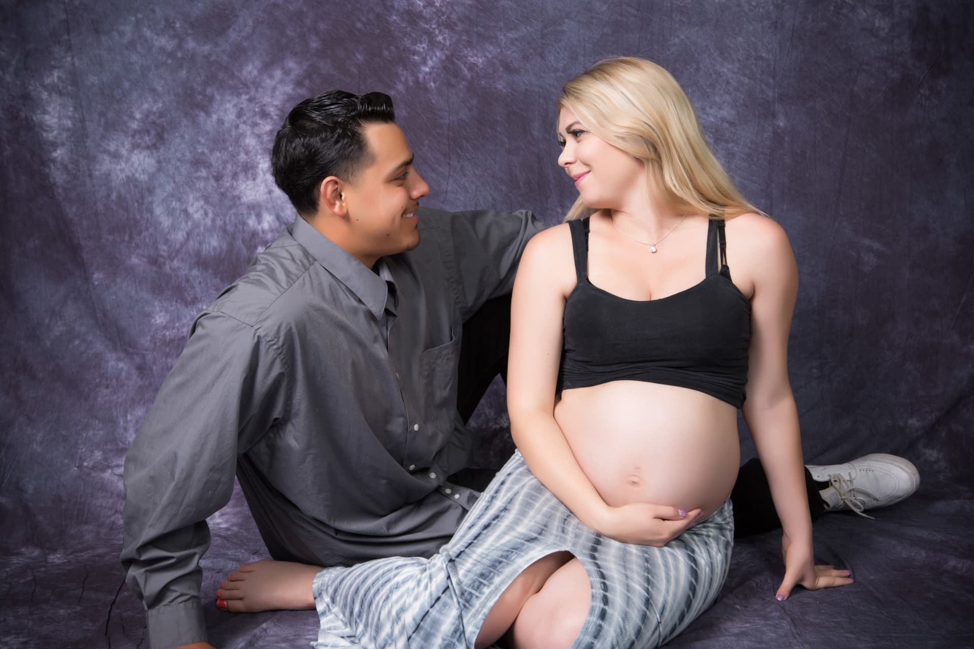 Expectant couple seated together and smiling at one another