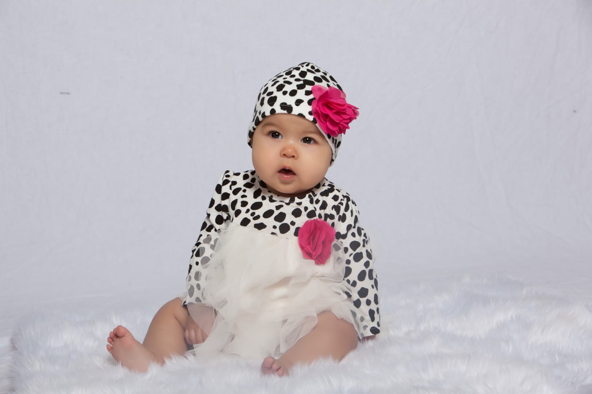 Baby girl seated in a spotted outfit with a bright pink flower