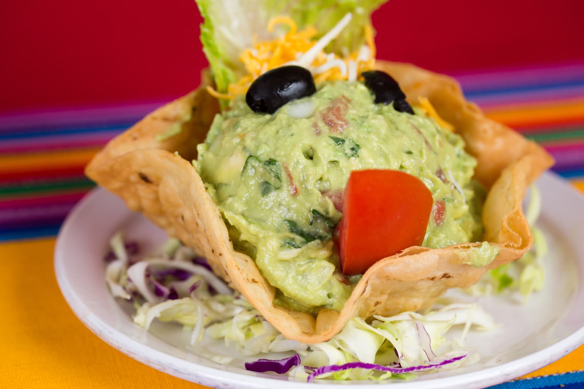 Fresh guacamole served in a crisp tortilla bowl with olives and tomato