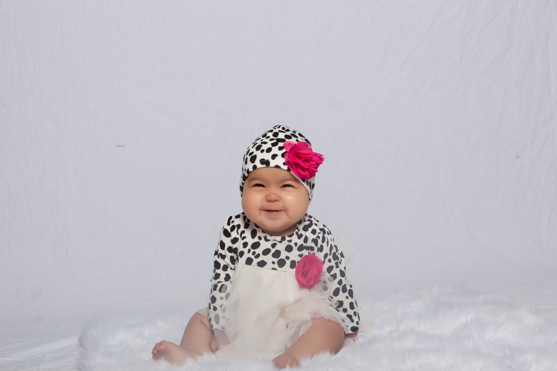 Smiling baby girl seated in a spotted outfit with a bright pink flower